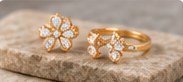 Two floral diamond rings in yellow gold on a stone surface